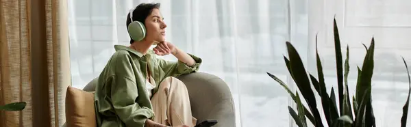 A woman sits in a comfortable armchair, wearing headphones and looking out the window. — Stock Photo