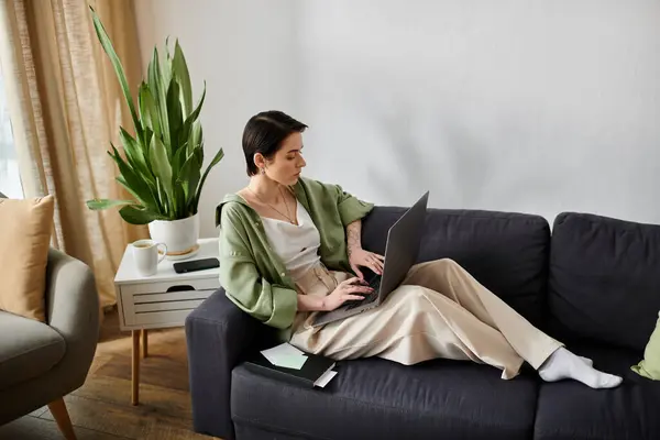 A woman sits on a couch in her home, working on a laptop. — Stock Photo