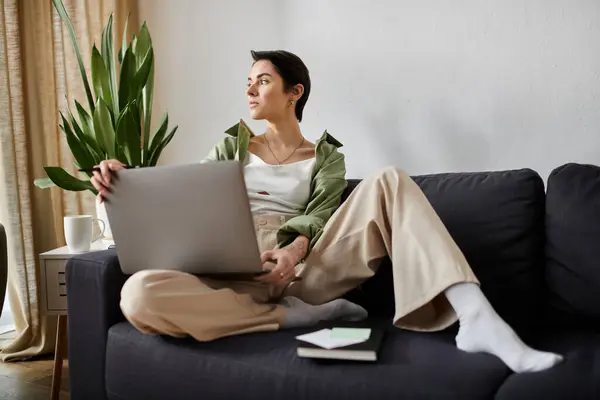 Uma mulher senta-se em um sofá em sua casa, trabalhando em um laptop. — Fotografia de Stock