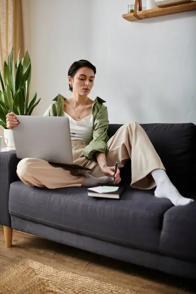 A woman works on her laptop while sitting on a couch in a comfortable home setting. — Stock Photo