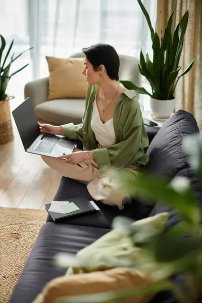 A woman sits on a couch, working on her laptop in her home. — Stock Photo