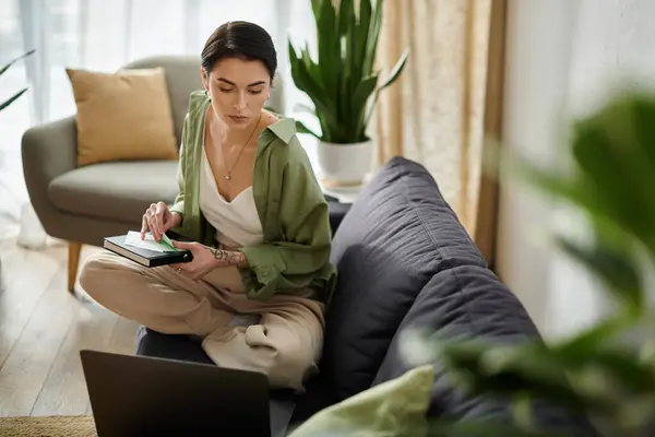 A young woman sits on a couch, reviewing documents while working from home. — Stock Photo
