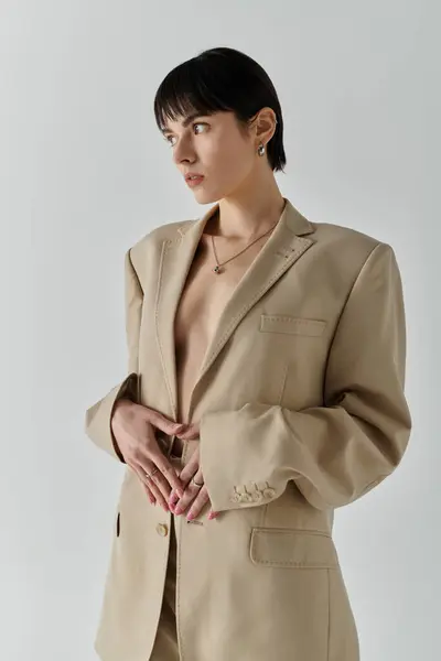 A woman in a tan blazer stands against a white wall. — Stock Photo