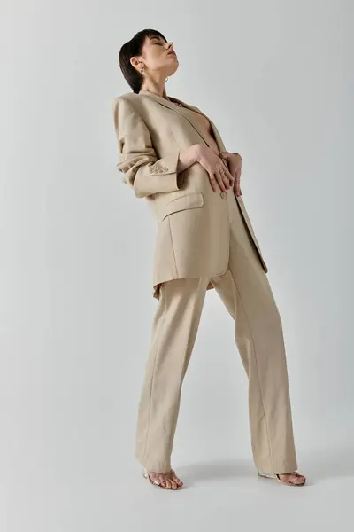 A woman wearing a tan suit and heels poses against a white backdrop. — Stock Photo