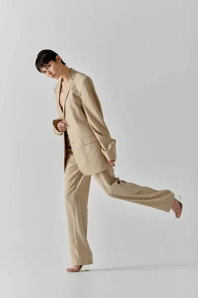 A young woman in a tan suit stands against a white background, posing with one leg extended. — Stock Photo