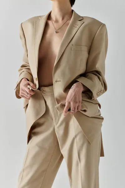 Una mujer con un traje bronceado se levanta sobre un fondo blanco, su chaqueta abierta. - foto de stock