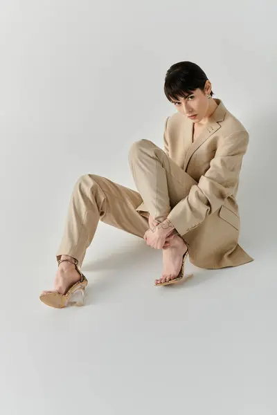 A woman in a beige suit sits on a plain white backdrop, looking down at her feet. — Stock Photo