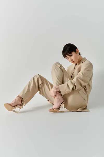 Une femme en costume beige s'assoit les jambes croisées, sur fond blanc. — Photo de stock