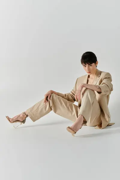 Une femme portant un costume beige et des talons clairs pose les jambes croisées sur un fond blanc. — Photo de stock
