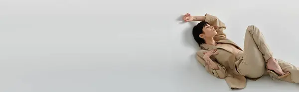 Uma jovem posa em um pano de fundo branco, vestindo um terno bege e deitada de lado. — Fotografia de Stock