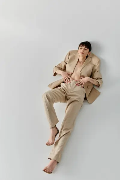 Woman in beige suit reclines on white background, legs outstretched, hands on waist. — Stock Photo