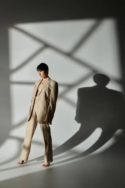 Woman in beige suit poses barefoot in a studio with geometric shadows on the wall. — Stock Photo