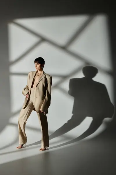A stylish woman in a tan suit poses in a studio with sunlight casting geometric shadows. — Stock Photo