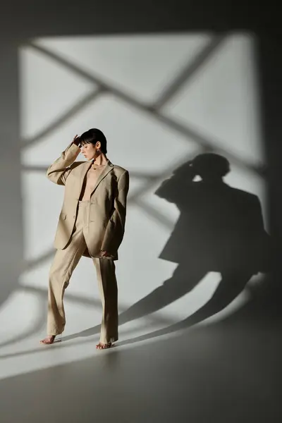 A woman in a beige suit poses against a white backdrop with geometric shadows. — Stock Photo