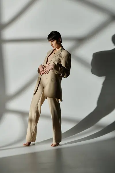 Woman in tan suit poses in front of white background, sunlight casting shadows. — Stock Photo