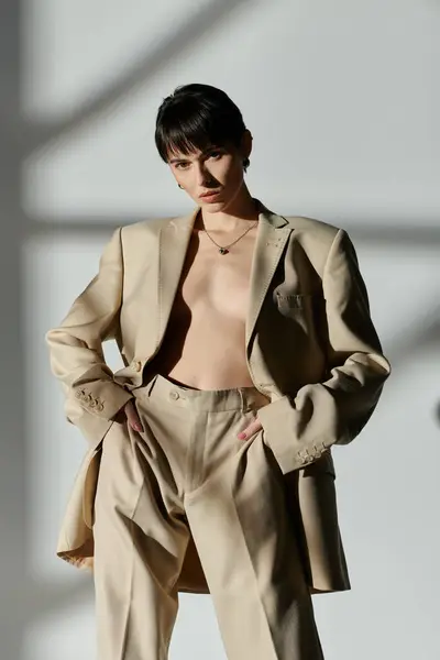 Woman in tan suit confidently poses against white wall, light streaming in, casting shadows. — Stock Photo