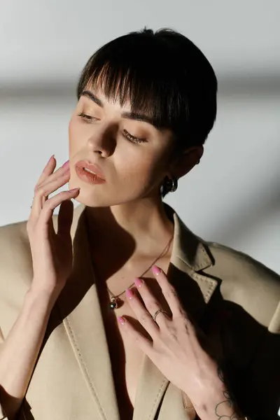 Una mujer con el pelo corto y oscuro posa elegantemente en una chaqueta beige sobre un fondo blanco. - foto de stock