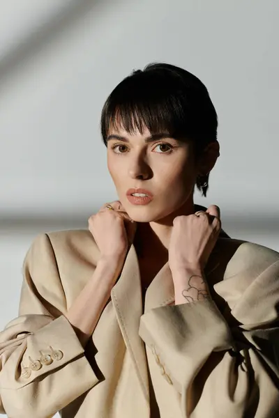 Una mujer con el pelo corto y oscuro posa en una chaqueta beige. - foto de stock