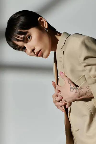 Una mujer con el pelo corto posa con confianza en una chaqueta beige sobre un fondo blanco. - foto de stock