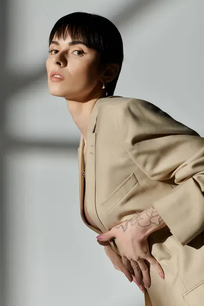 Uma mulher com cabelo escuro curto e um blazer bege posa contra um pano de fundo branco. — Fotografia de Stock