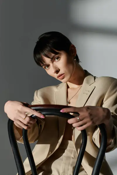 Una mujer atractiva con una chaqueta beige posa mientras está sentada en una silla. - foto de stock