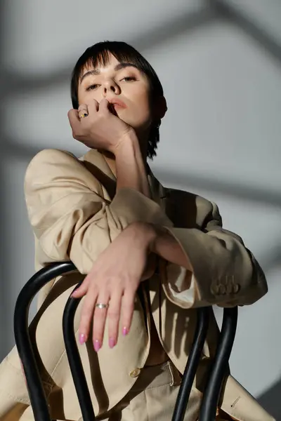 A young woman wearing a tan suit and sitting on a chair in a studio. — Stock Photo