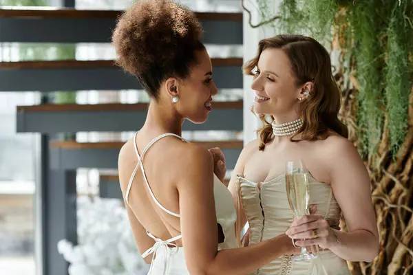 Duas noivas em vestidos brancos compartilham um brinde e um sorriso no dia do casamento. — Fotografia de Stock