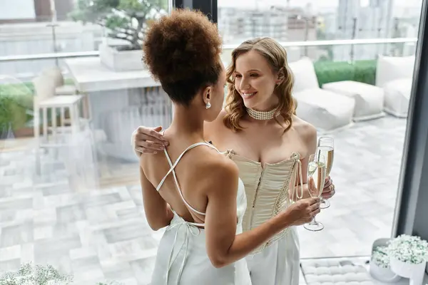 Duas noivas em vestidos brancos torram um a outro com a champanha em um telhado. — Fotografia de Stock