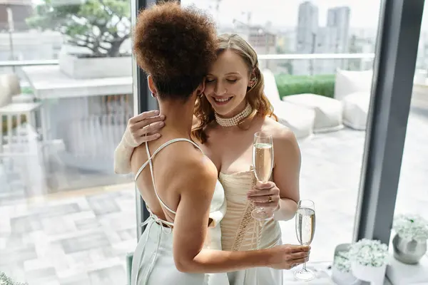Una pareja de lesbianas abraza y hace un brindis el día de su boda, mirando el horizonte de la ciudad. - foto de stock