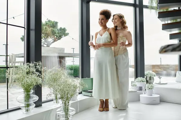 Lesbian couple in white celebrating wedding with champagne in modern space. — Stock Photo