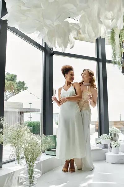 Two brides in white dresses toast their love on wedding day by an ocean view. — Stock Photo