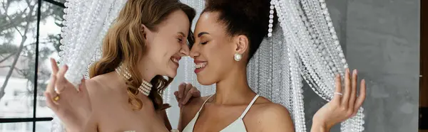 Una pareja lesbiana, vestida de blanco, se sonríen durante la ceremonia de su boda. - foto de stock