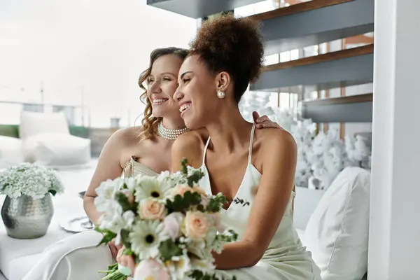 Two brides smiling tenderly, gazing out a window on their wedding day. — Stock Photo