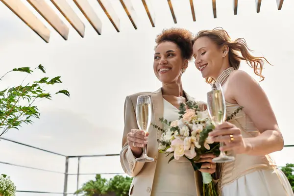 Две невесты разделяют любящий момент во время их свадебной церемонии, поднимая тост с шампанским. — стоковое фото