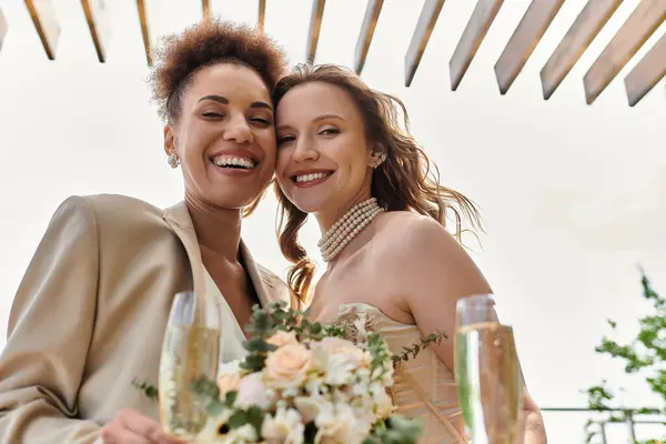 A lesbian couple toasts to their wedding day, smiling and happy under a wooden pergola. — Stock Photo