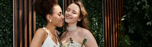 Two brides embrace on their wedding day, surrounded by greenery. — Stock Photo