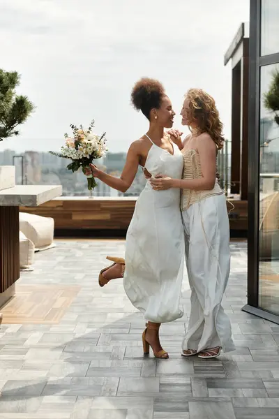 Two brides in white wedding attire stand on a rooftop, smiling and holding hands. — Stock Photo