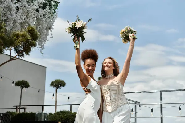 Two brides celebrate their wedding on a rooftop, holding bouquets and smiling. — Stock Photo