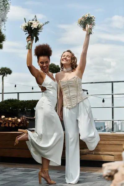 Two brides in white dresses celebrate their wedding on a rooftop terrace. — Stock Photo