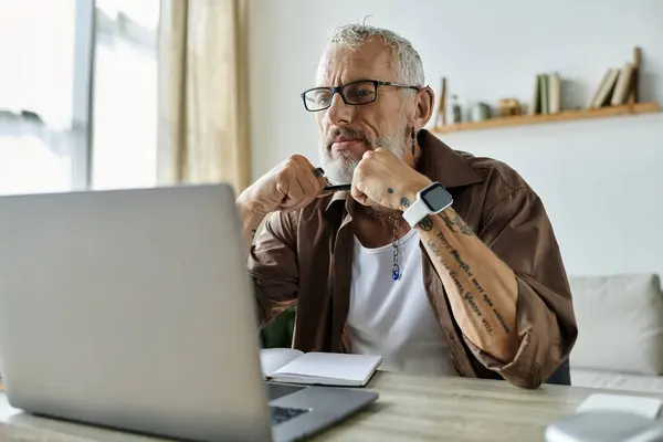 A mature gay man with tattoos and grey hair works remotely from home on a laptop. — Stock Photo
