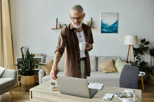 Ein reifer Mann mit Tätowierungen und grauen Haaren arbeitet fernab von zu Hause und macht eine Pause, um eine Tasse Kaffee zu genießen. — Stockfoto