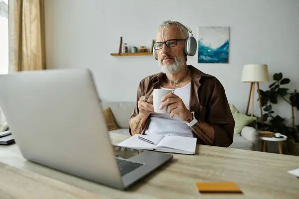 A mature gay man with tattoos and grey hair works remotely from home, enjoying a cup of coffee and the tranquility of his surroundings. — Stock Photo