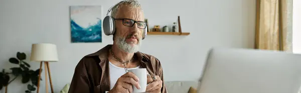 A mature gay man with tattoos and grey hair works remotely from his home office. — Stock Photo