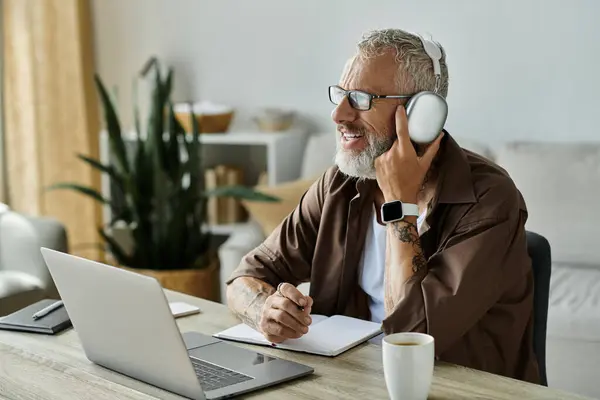 A mature, tattooed gay man works remotely from home, wearing headphones and glasses. — Stock Photo