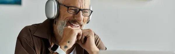 Un homme gay mature avec des tatouages et des cheveux gris sourit tout en travaillant à la maison. — Photo de stock