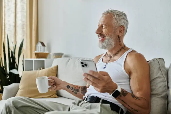 A mature gay man with tattoos and a grey beard relaxes on his couch, enjoying a moment of peace at home. — Stock Photo