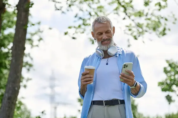 A mature gay man with tattoos and a grey beard smiling and looking at his phone. — Stock Photo