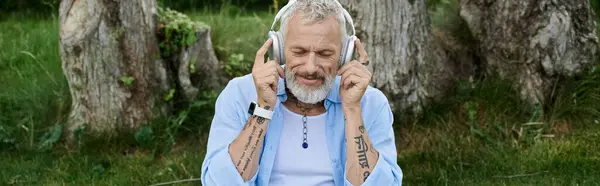 A tattooed, bearded gay man relaxes on grass, listening to music outdoors. — Stock Photo