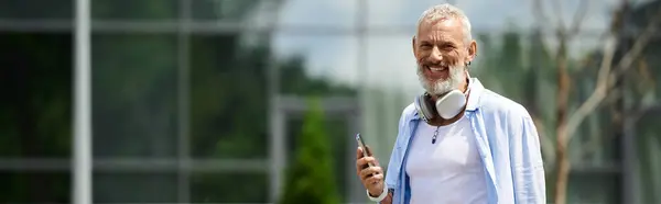 A mature gay man with tattoos and a grey beard smiles as he stands outdoors. — Stock Photo