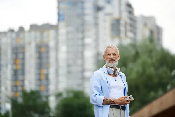 A mature man with tattoos and a grey beard standing in an urban setting. — Stock Photo